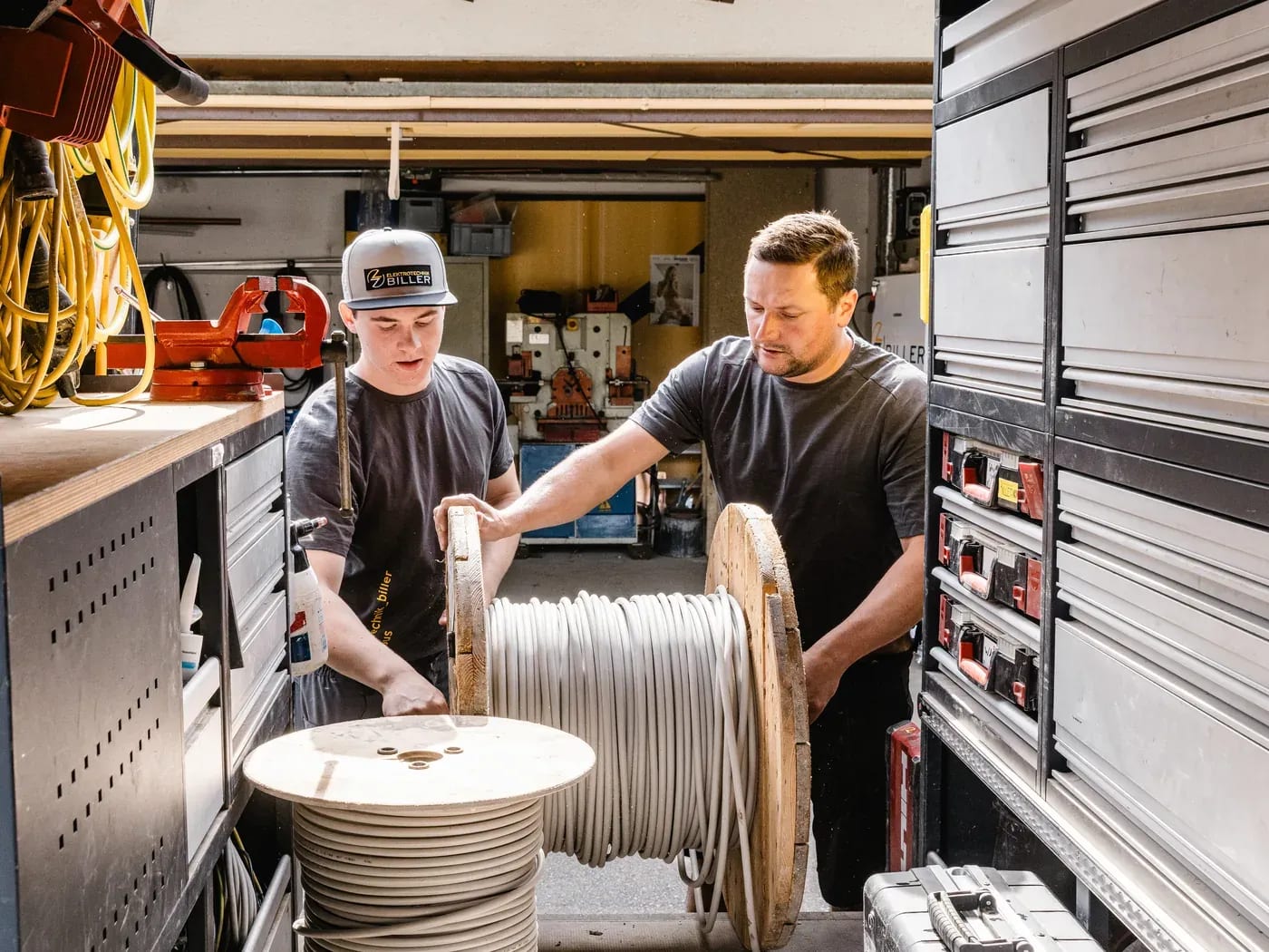Zwei Mitarbeiter verladen eine Kabeltrommel im ausgebauten Werkstattfahrzeug